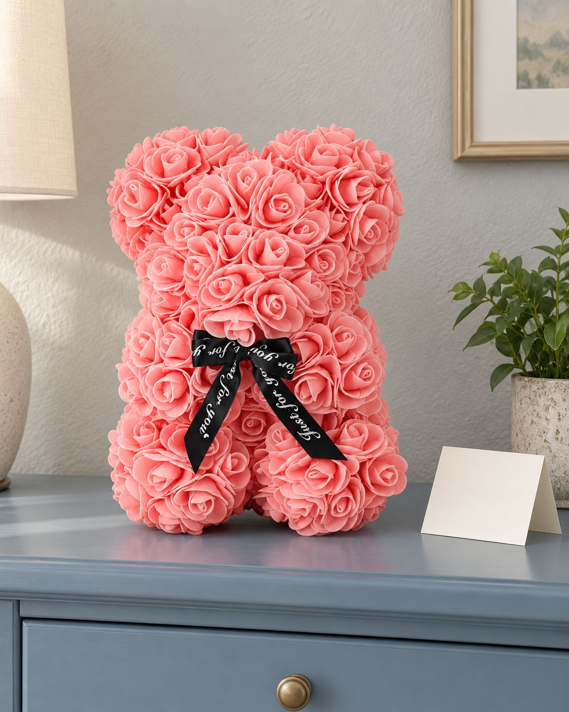 Teddy bear covered in roses, sitting on a dresser beside a blank card