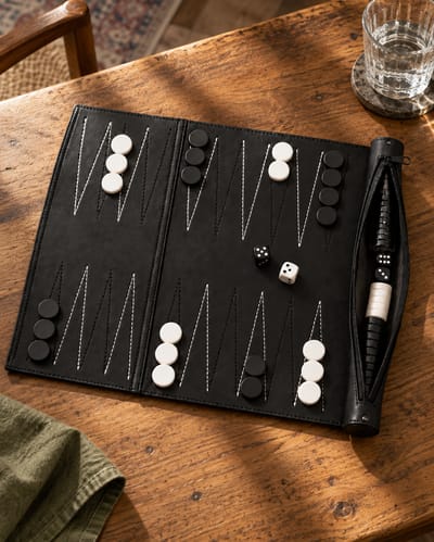 Black roll-up backgammon set with checkers on muted warm olive linen