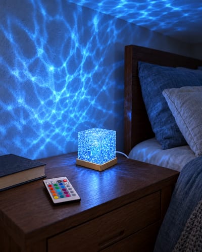 Cube lamp glowing blue on a bedside table, with its remote beside it.