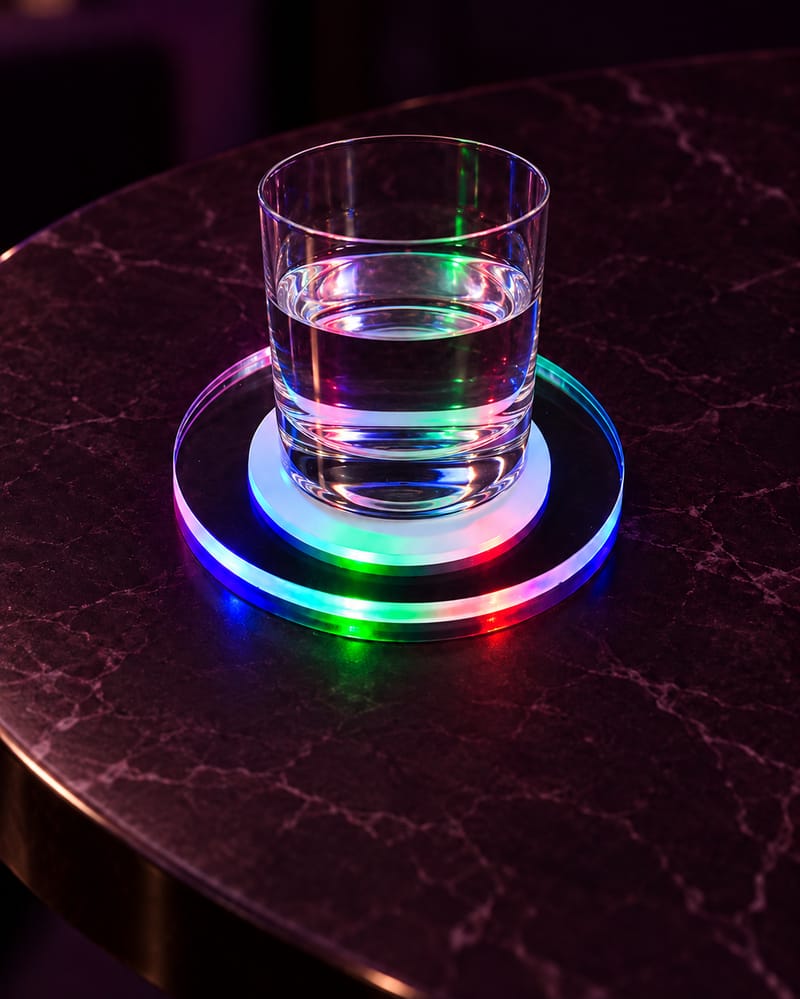 Illuminated LED coaster supporting a clear glass of water